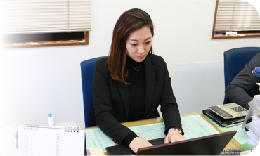 手帳とEメールでスケジュールのチェックを行う谷村 文